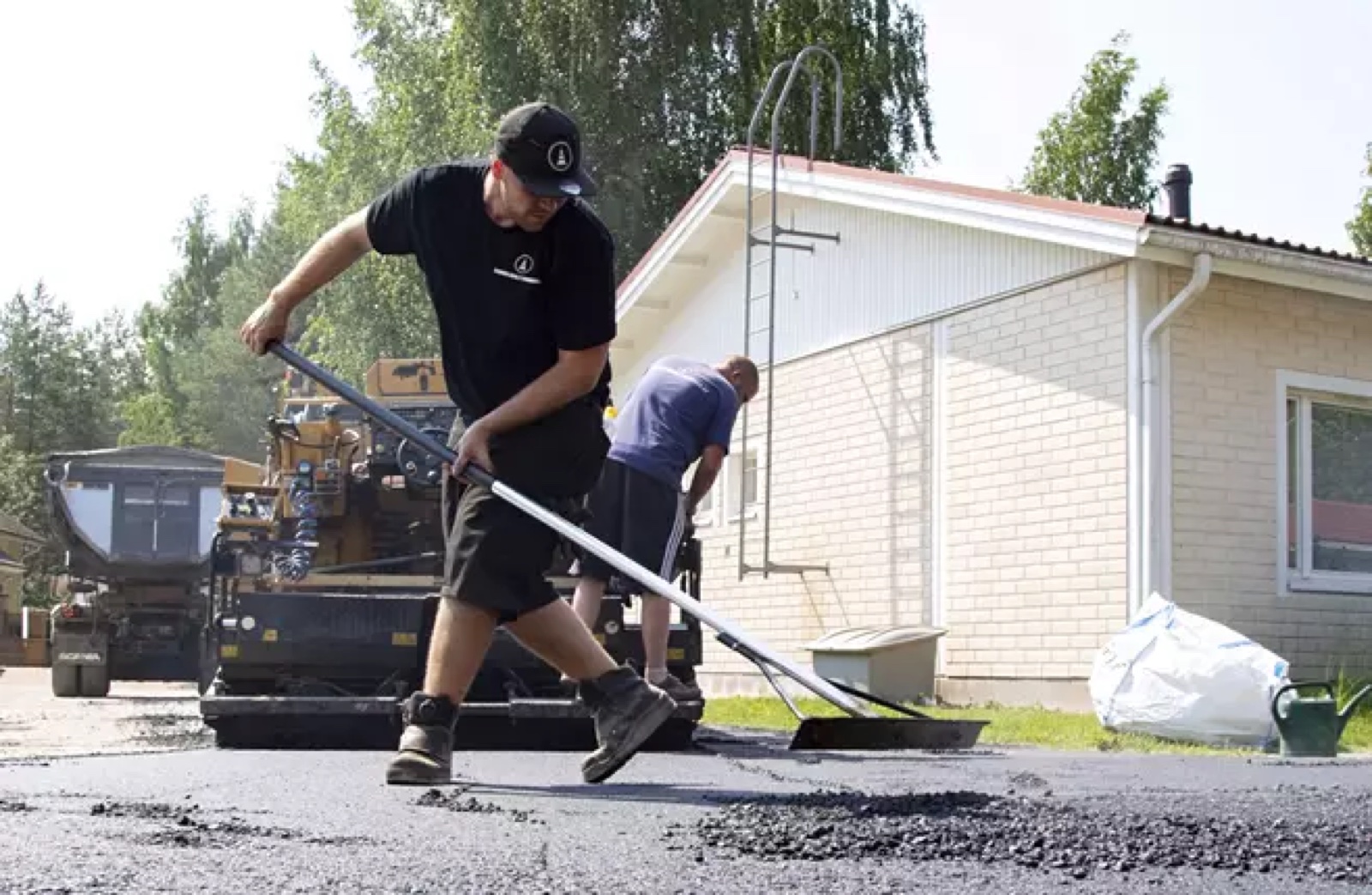 Asfalttityöntekijä viimeistelee asfalttipintaa levittimen edessä