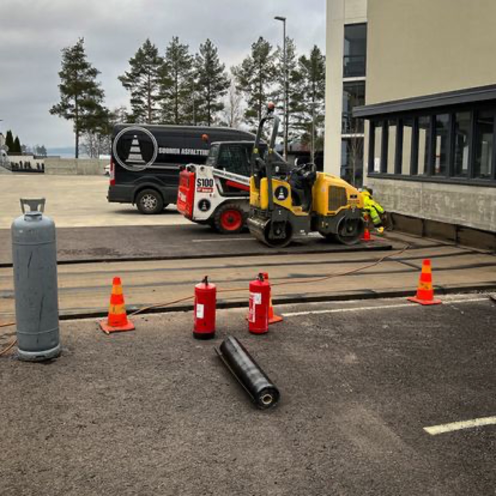 Bitumityö rakennuksen vierustalla työmaakaluston avulla